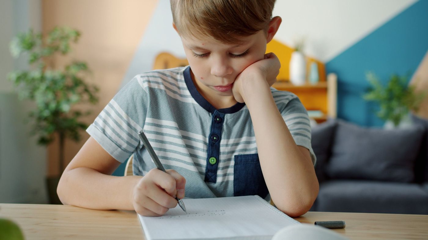 A boy resting his chin on his hand as he writes in his homework notebook