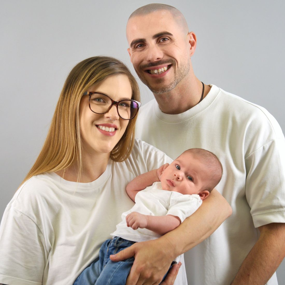 A smiling mother and father holding their newborn baby together