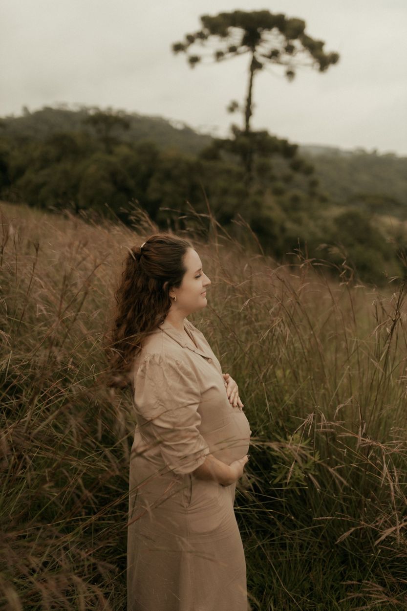 A pregnant woman standing in tall grass, hands on her belly, smiling