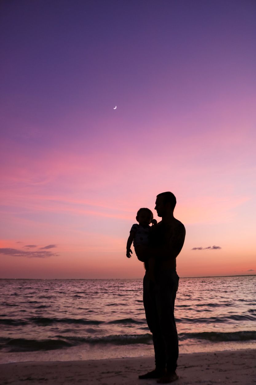 A father holding his small child by the sea at sunset