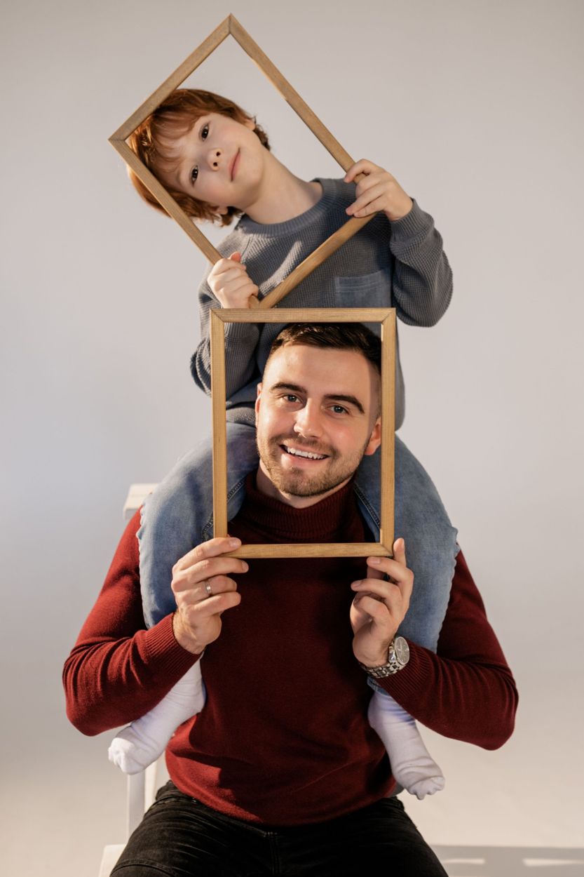 A smiling father carrying his son on his shoulders, both holding up wooden picture frames