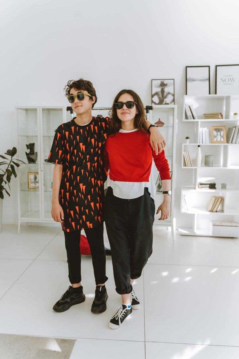 A mother and her teenage son standing arm in arm at home, both in sunglasses